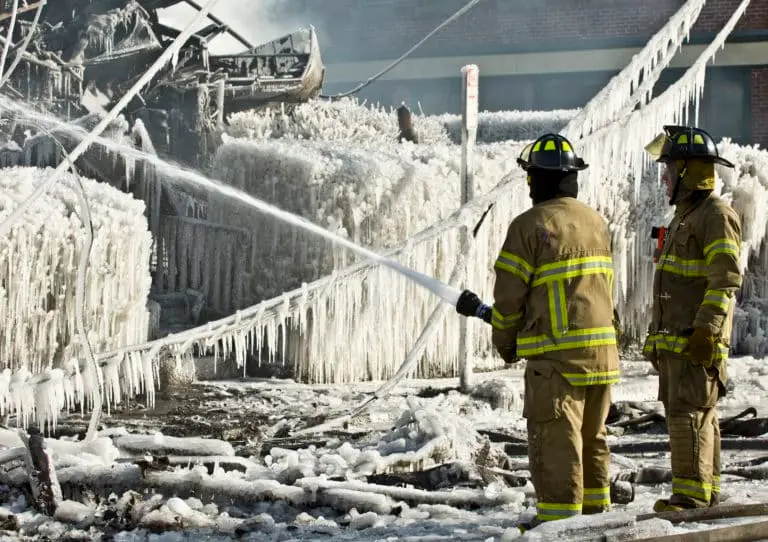 Firefighters battle an icy blaze, with water frozen mid-air by frigid temperatures, encapsulating the scene in a frozen cascade.
